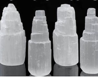 May include: Several white selenite tower crystals of varying sizes are displayed against a black background. The crystals have a layered appearance, with a rough, textured surface. The crystals are arranged in a row, showcasing their unique shapes and sizes.