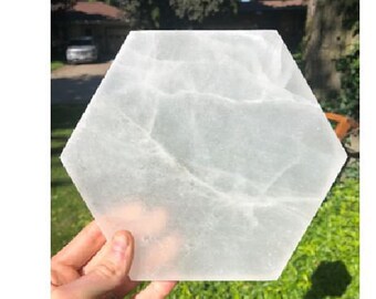 May include: A white selenite charging plate with a hexagonal shape. The plate has a smooth, polished surface with natural veining.
