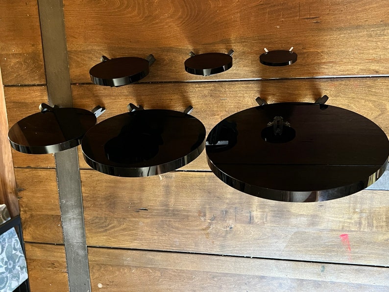 Peut inclure: Cinq &eacute;tag&egrave;res circulaires noires mont&eacute;es sur un mur en bois. Les &eacute;tag&egrave;res sont de tailles diff&eacute;rentes et sont toutes en mat&eacute;riau brillant.