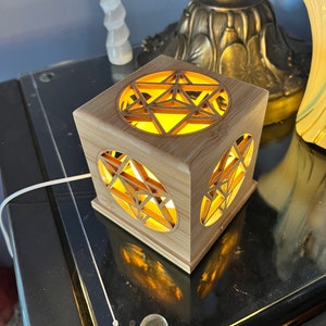May include: A wooden cube nightlight with a geometric star design. The light shines through the cutouts in the wood, creating a warm glow.