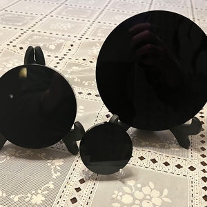 Peut inclure: Trois miroirs circulaires en verre ou en acrylique noir de diff&eacute;rentes tailles sur des supports noirs. Les miroirs sont sur une nappe en dentelle blanche.