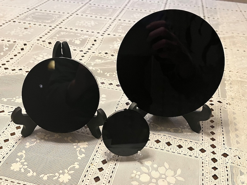 Peut inclure: Trois miroirs circulaires en verre ou en acrylique noir de diff&eacute;rentes tailles sur des supports noirs. Les miroirs sont sur une nappe en dentelle blanche.
