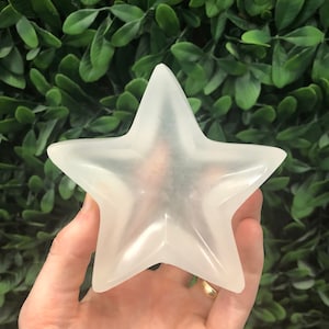 Puede incluir: Un cristal de selenita blanco en forma de estrella. El cristal es liso y pulido, con una apariencia translúcida.