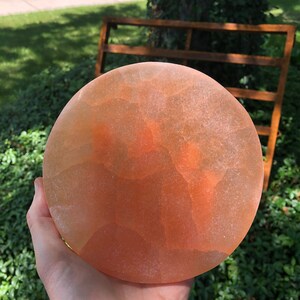 May include: A round, orange-colored, translucent, salt plate with a rough, textured surface.