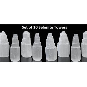 May include: Set of 10 white selenite crystal towers. Each tower is a different size and has a unique shape. The towers are arranged in a row on a black background.