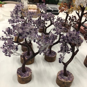 May include: Multiple amethyst crystal trees on wooden bases. The trees are made of wire and amethyst crystals. The crystals are a light purple color.