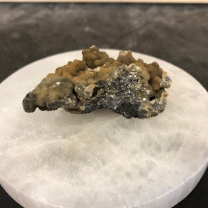 May include: A cluster of brown and gray mineral specimens on a white circular surface.