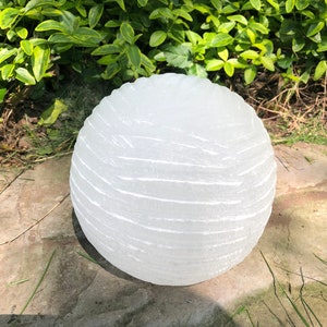 May include: A white, round, textured salt lamp with a smooth, polished surface. The lamp is sitting on a stone surface.