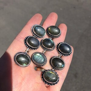 May include: A collection of eight silver rings with oval-shaped labradorite gemstones. The rings have a beaded edge and a silver band.