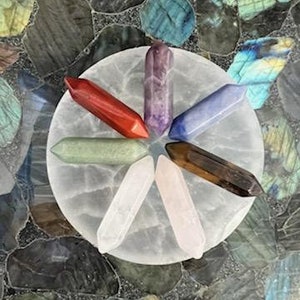 May include: Seven crystal points in various colors, including red, green, purple, blue, brown, clear, and pink, are arranged in a star shape on a white circular base.