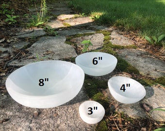 May include: Four white selenite bowls of varying sizes, 3 inches, 4 inches, 6 inches, and 8 inches in diameter. The bowls are arranged on a stone path covered in moss.