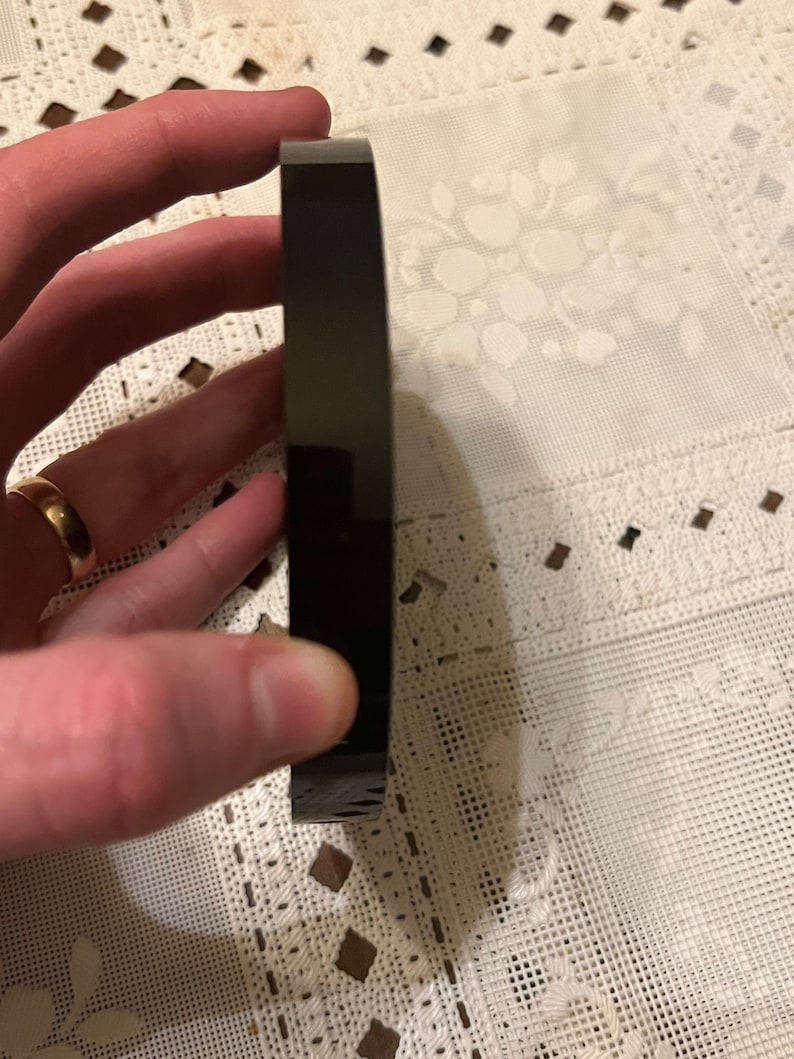 Peut inclure: Un objet rond noir avec une surface lisse et brillante. L'objet est tenu par une main.