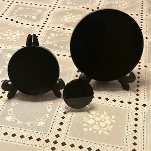 Peut inclure: Trois disques circulaires noirs de tailles diff&eacute;rentes sur des supports en dentelle blanche. Les disques sont en pierre noire polie et sont expos&eacute;s sur une nappe en dentelle blanche.
