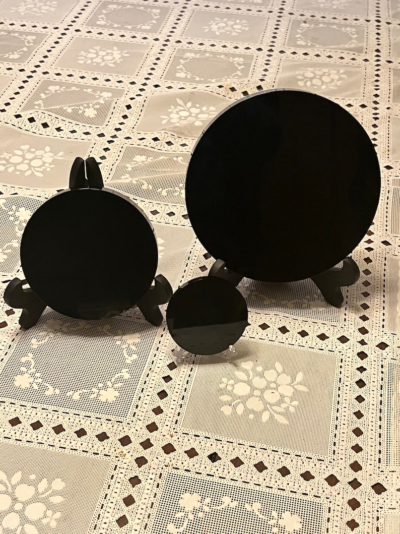 Peut inclure: Trois disques circulaires noirs de tailles diff&eacute;rentes sur des supports en dentelle blanche. Les disques sont en pierre noire polie et sont expos&eacute;s sur une nappe en dentelle blanche.