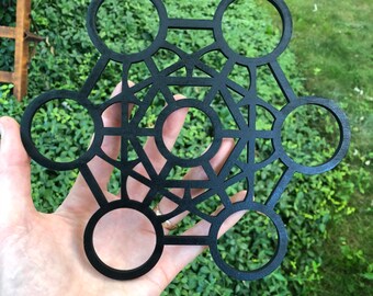 May include: Black wooden geometric mandala with a circular design. The mandala is made of multiple overlapping circles and lines.