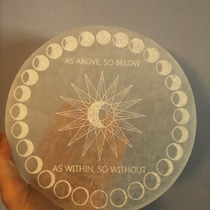 May include: A white circular selenite plate with a sun and moon design and the text "As Above, So Below" and "As Within, So Without". The plate is surrounded by a circle of moon phases.