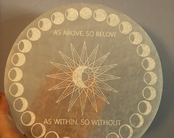 May include: A white circular selenite plate with a sun and moon design and the text "As Above, So Below" and "As Within, So Without". The plate is surrounded by a circle of moon phases.