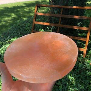 May include: A round, light pink Himalayan salt plate. The plate is smooth and has a slightly textured surface.