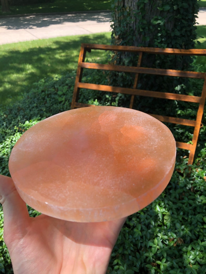 May include: A round, light pink Himalayan salt plate. The plate is smooth and has a slightly textured surface.