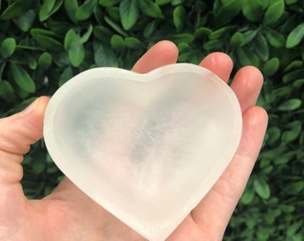 May include: A white heart-shaped selenite bowl. The bowl is smooth and polished, with a slightly translucent appearance.