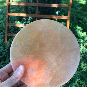 May include: A round, translucent, orange and yellow disc with a rough texture. The disc is being held in a hand.