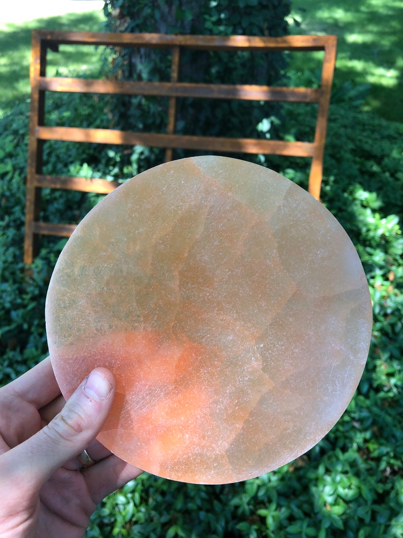 May include: A round, translucent, orange and yellow disc with a rough texture. The disc is being held in a hand.