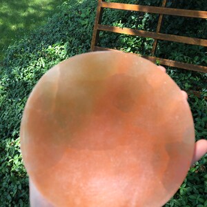 May include: A large, round, pink Himalayan salt bowl. The bowl is smooth and has a slight orange hue.
