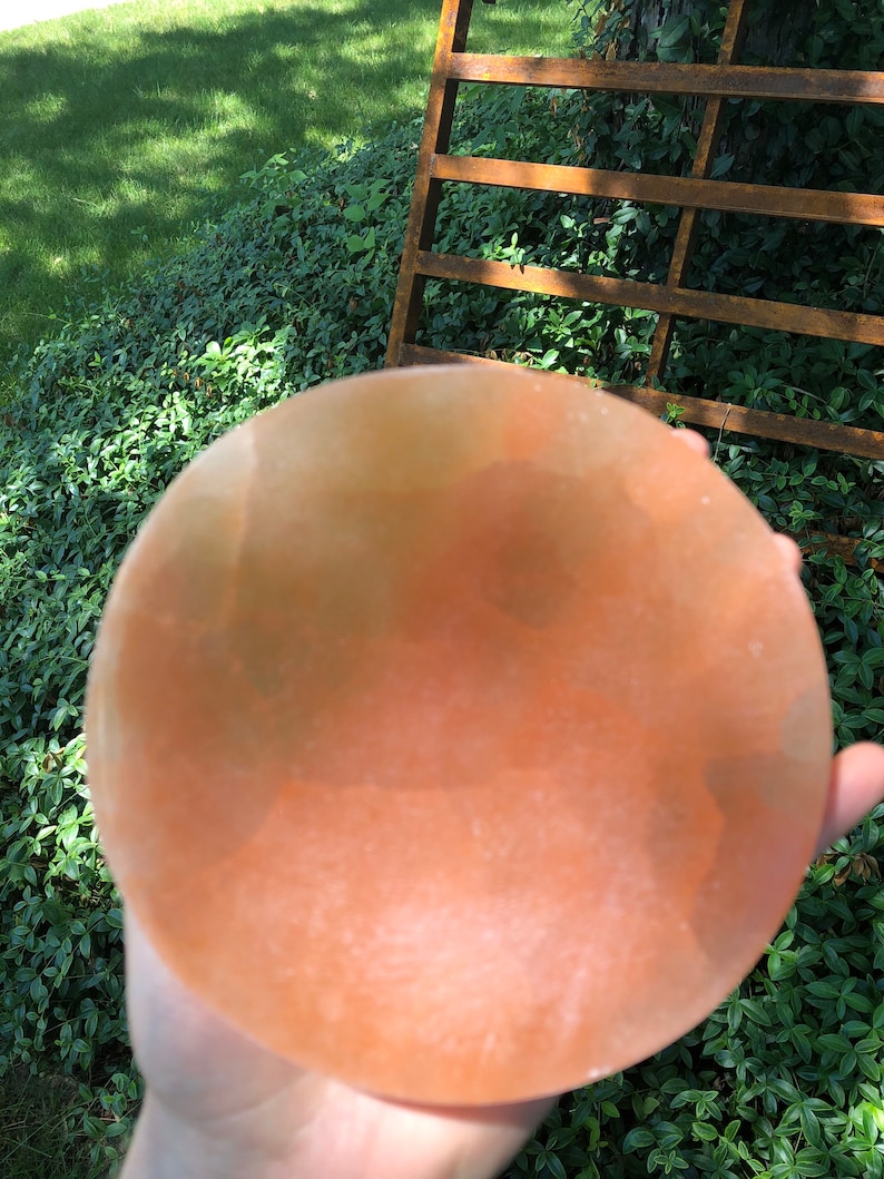 May include: A large, round, pink Himalayan salt bowl. The bowl is smooth and has a slight orange hue.