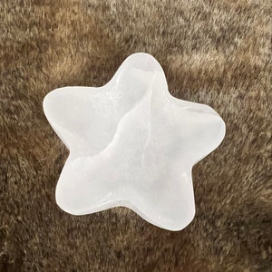 Puede incluir: Un cristal de selenita blanco en forma de estrella sobre una superficie marrón y peluda.
