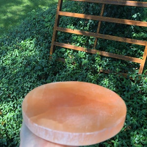 May include: A large, round, light pink Himalayan salt plate. The plate is smooth and has a slightly textured surface.