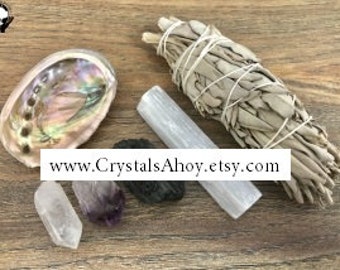 May include: A set of crystals for cleansing and meditation, including a white selenite stick, a black obsidian crystal, an amethyst crystal, a white crystal, a bundle of white sage, and an abalone shell.