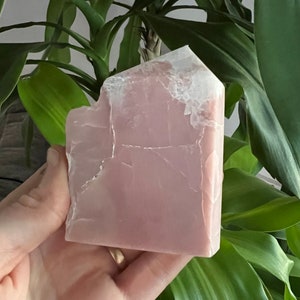 May include: A large, pink, natural crystal with a rough, irregular shape. The crystal has a translucent, milky appearance with white veins running through it.