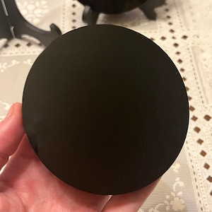 Peut inclure: Un disque circulaire noir, possiblement en obsidienne ou un mat&eacute;riau similaire, est tenu dans une main. Le disque est lisse et r&eacute;fl&eacute;chissant.