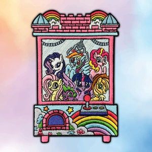 May include: Embroidered patch featuring a pink arcade claw machine design. The machine is filled with colorful cartoon ponies. The patch has a rainbow, stars, and a castle-like top. The design is outlined in black.