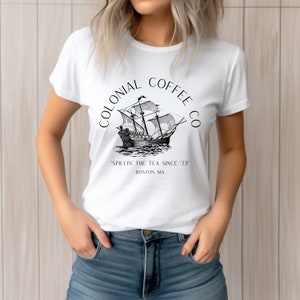 May include: White t-shirt featuring a black and white illustration of a tall ship with the text "COLONIAL COFFEE CO" above and "'SPILLIN' THE TEA SINCE '73" and "BOSTON, MA" below the ship.