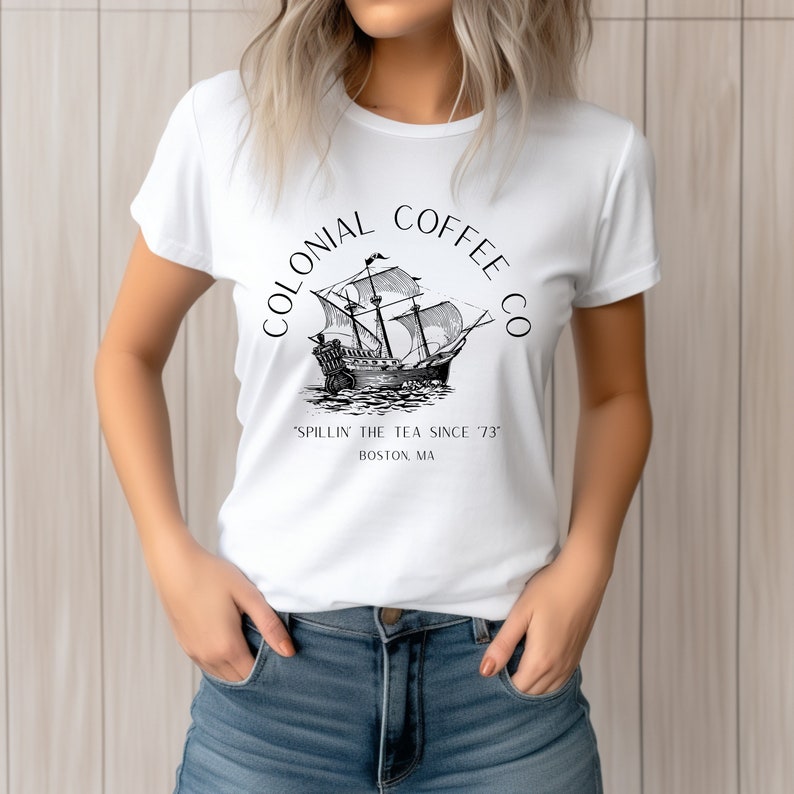 May include: White t-shirt featuring a black and white illustration of a tall ship with the text "COLONIAL COFFEE CO" above and "'SPILLIN' THE TEA SINCE '73" and "BOSTON, MA" below the ship.