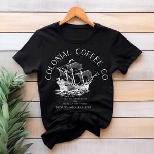 May include: Black t-shirt with a white graphic of a sailing ship and the text "COLONIAL COFFEE CO." The shirt also includes the text "I LIKE MY COFFEE BLACK AND MY TEA IN THE HARBOR BOSTON, MA &bull; EST. 1773."