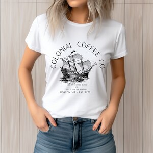 May include: White t-shirt featuring a black and white illustration of a tall ship with the text "COLONIAL COFFEE CO." above it. Below the ship, the text reads "I LIKE MY COFFEE BLACK AND MY TEA IN THE HARBOR BOSTON, MA &bull; EST. 1773."