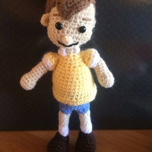 May include: A crocheted doll with brown hair, a yellow shirt, blue shorts, and brown shoes.