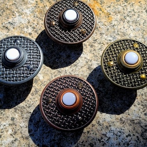 May include: Four round doorbells with a mesh design and a white button in the center. The doorbells have different metal finishes: silver, bronze, copper, and brass. Small screws are visible around the edges.