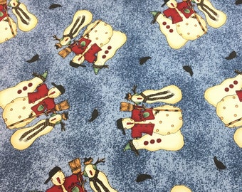 May include: A blue fabric with a repeating pattern of cream-colored snowmen wearing red jackets, black hats, and green earmuffs. Each snowman holds a brown broom, and the background features a speckled, textured blue design.