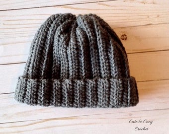 May include: A gray, ribbed knit beanie hat with a folded brim. The hat is made of a soft, textured yarn and is designed for warmth and comfort. The words "Cute & Cozy Crochet" are in the bottom right corner.