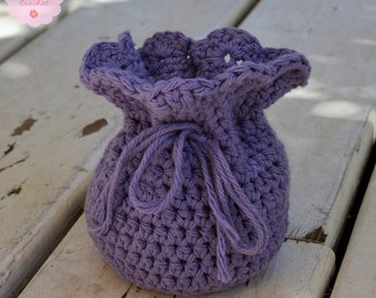 May include: A purple crocheted drawstring bag with a scalloped top. The bag is tied with a purple cord and is sitting on a white wooden surface.