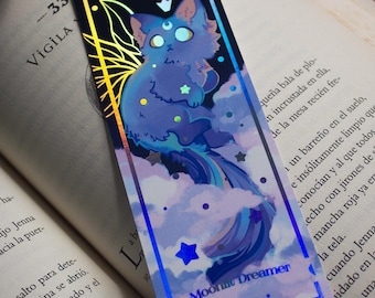 May include: A holographic bookmark featuring a blue cat with a crescent moon and stars on a cloudy background. The text "Moon Dreamer" is printed on the bookmark.