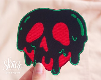 May include: A black and red embroidered patch shaped like a dripping apple with a skull face. The apple is outlined in green.