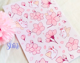 May include: A sheet of stickers featuring pink cherry blossoms and white bunnies with wings. The stickers are on a pink background with white outlines. The text "Shiro Create" is in the bottom left corner.