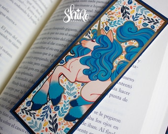 May include: A blue and gold bookmark featuring a unicorn with a blue mane and tail. The unicorn is surrounded by a floral pattern with leaves and flowers in shades of blue, green, yellow, and orange.