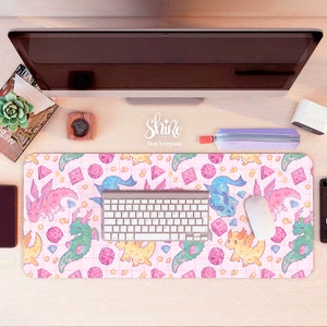 Puede incluir: Una alfombrilla de escritorio rosa y blanca con un patrón de cuadrícula y un diseño repetido de dragones y dados coloridos. El texto "Shiro Don't repost" está impreso en el centro de la alfombrilla.