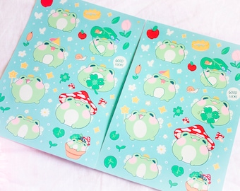 May include: A sheet of stickers featuring cute green frogs with wings, hats, and other whimsical details. The stickers are on a light blue background with white stars, flowers, and other designs. The text "Good Luck!" appears on the sheet.
