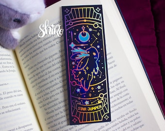 May include: A black bookmark with a holographic design featuring a rabbit, stars, and a crescent moon. The text "STAR JUMPER" is displayed on a banner. The bookmark is placed in an open book.